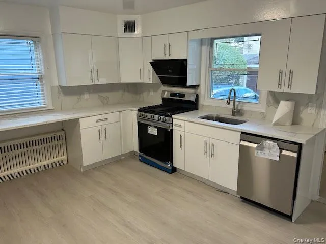 Kitchen with stainless steel appliances, radiator heating unit, light stone counters, and light wood-style floors Kitchen with stainless steel appliances, radiator heating unit, light stone counters, and light wood-style floors