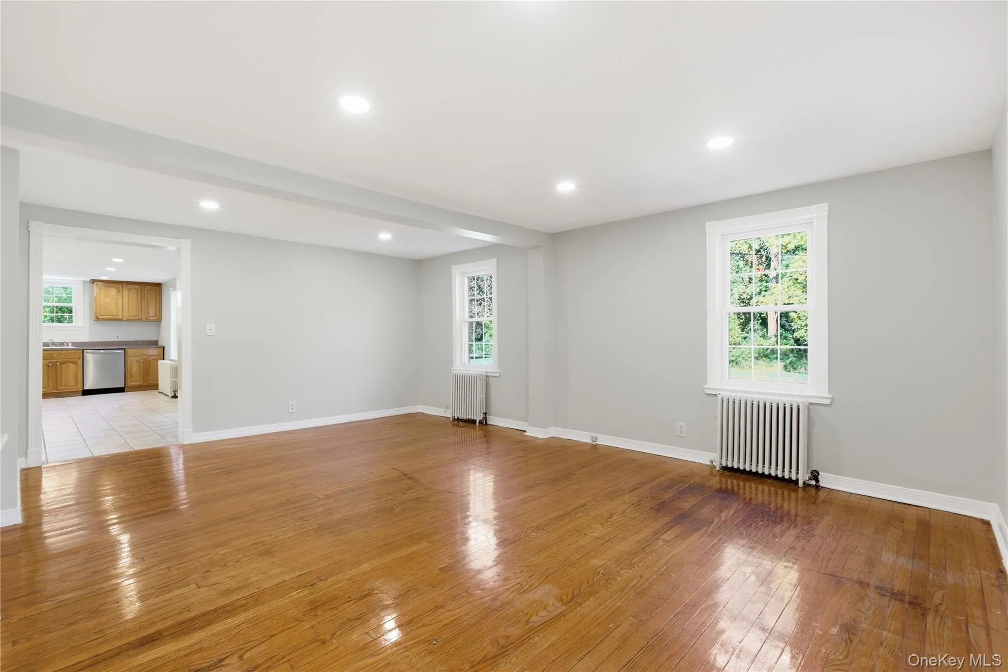 Empty room with light wood finished floors, radiator heating unit, recessed lighting, and plenty of natural light Empty room with light wood finished floors, radiator heating unit, recessed lighting, and plenty of natural light