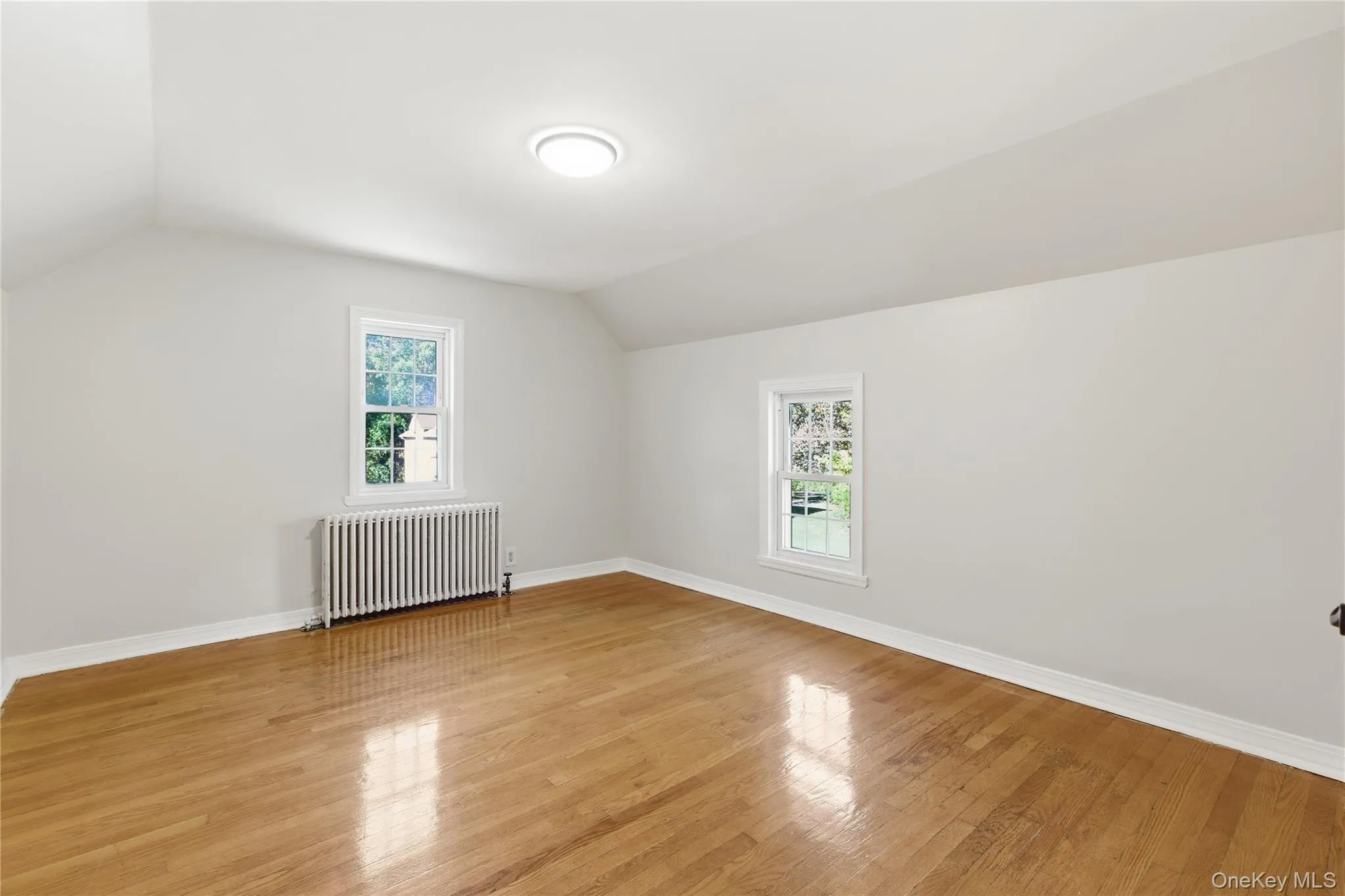 Additional living space with vaulted ceiling, radiator heating unit, and light wood-style flooring Additional living space with vaulted ceiling, radiator heating unit, and light wood-style flooring