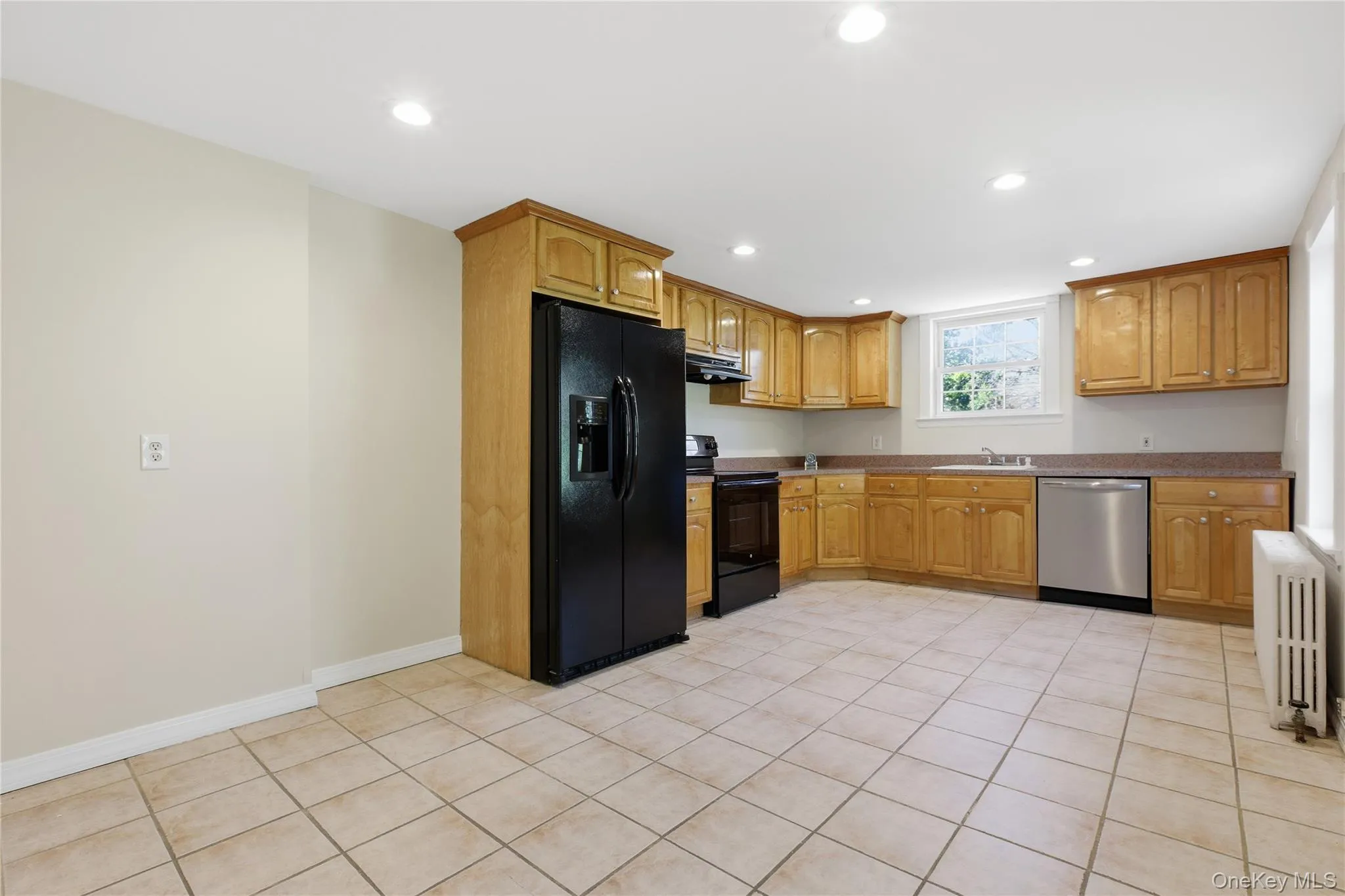 Kitchen featuring black appliances, light tile patterned floors, radiator, recessed lighting, and under cabinet range hood Kitchen featuring black appliances, light tile patterned floors, radiator, recessed lighting, and under cabinet range hood
