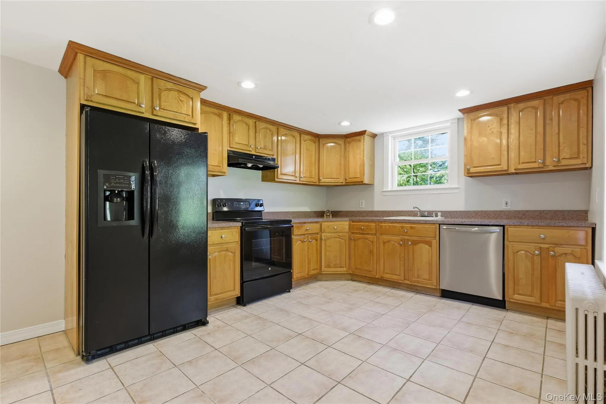 Kitchen with black appliances, radiator heating unit, light tile patterned flooring, recessed lighting, and under cabinet range hood Kitchen with black appliances, radiator heating unit, light tile patterned flooring, recessed lighting, and under cabinet range hood