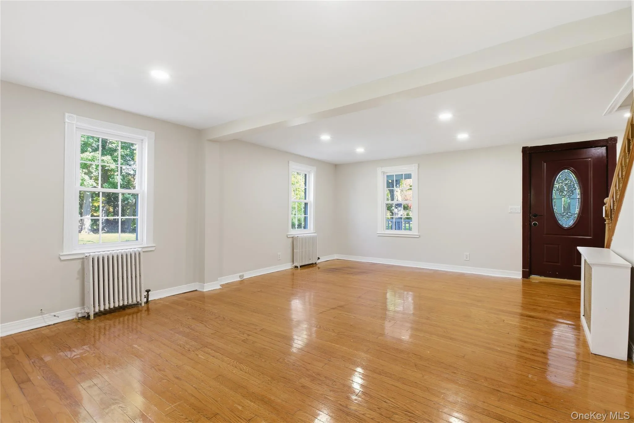 Unfurnished living room with radiator, light wood-type flooring, plenty of natural light, and recessed lighting Unfurnished living room with radiator, light wood-type flooring, plenty of natural light, and recessed lighting