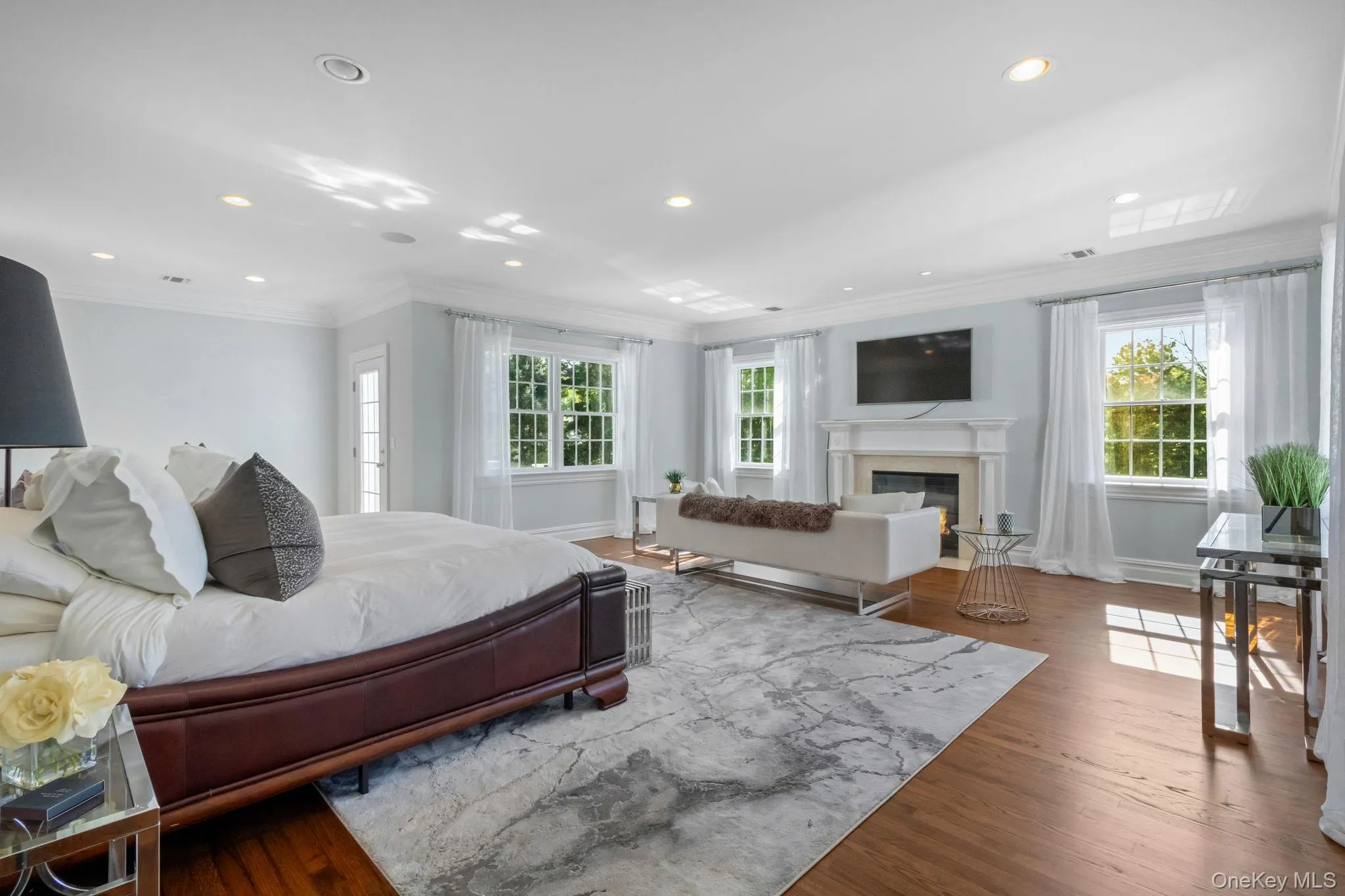 Bedroom featuring ornamental molding, multiple windows, recessed lighting, a high end fireplace, and wood finished floors Bedroom featuring ornamental molding, multiple windows, recessed lighting, a high end fireplace, and wood finished floors