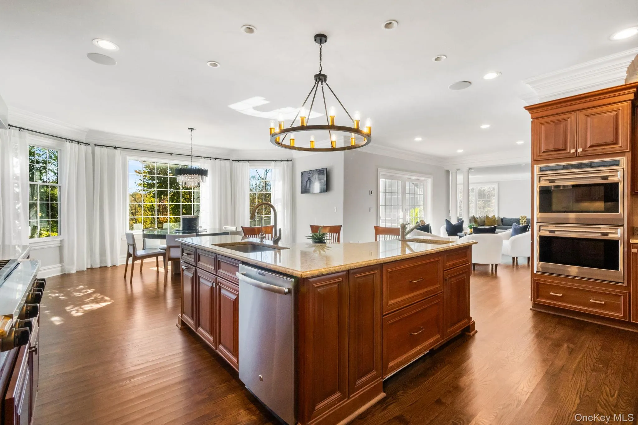 Kitchen featuring brown cabinets, ornamental molding, light stone countertops, a chandelier, and stainless steel appliances Kitchen featuring brown cabinets, ornamental molding, light stone countertops, a chandelier, and stainless steel appliances
