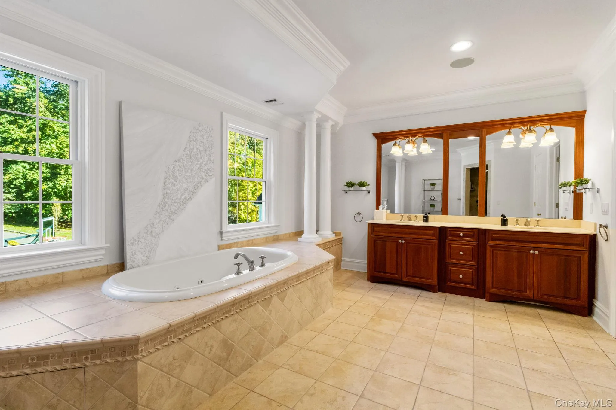 Full bathroom featuring double vanity, a tub with jets, ornamental molding, light tile patterned floors, and a chandelier Full bathroom featuring double vanity, a tub with jets, ornamental molding, light tile patterned floors, and a chandelier