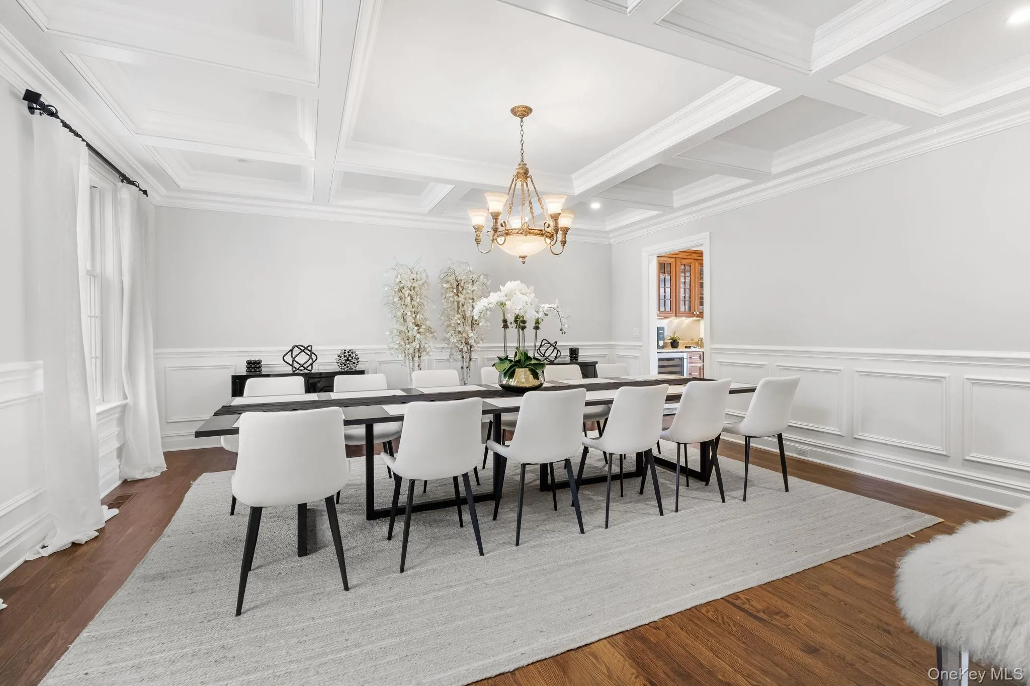 Dining area featuring beam ceiling, dark wood-style floors, a chandelier, a decorative wall, and coffered ceiling Dining area featuring beam ceiling, dark wood-style floors, a chandelier, a decorative wall, and coffered ceiling