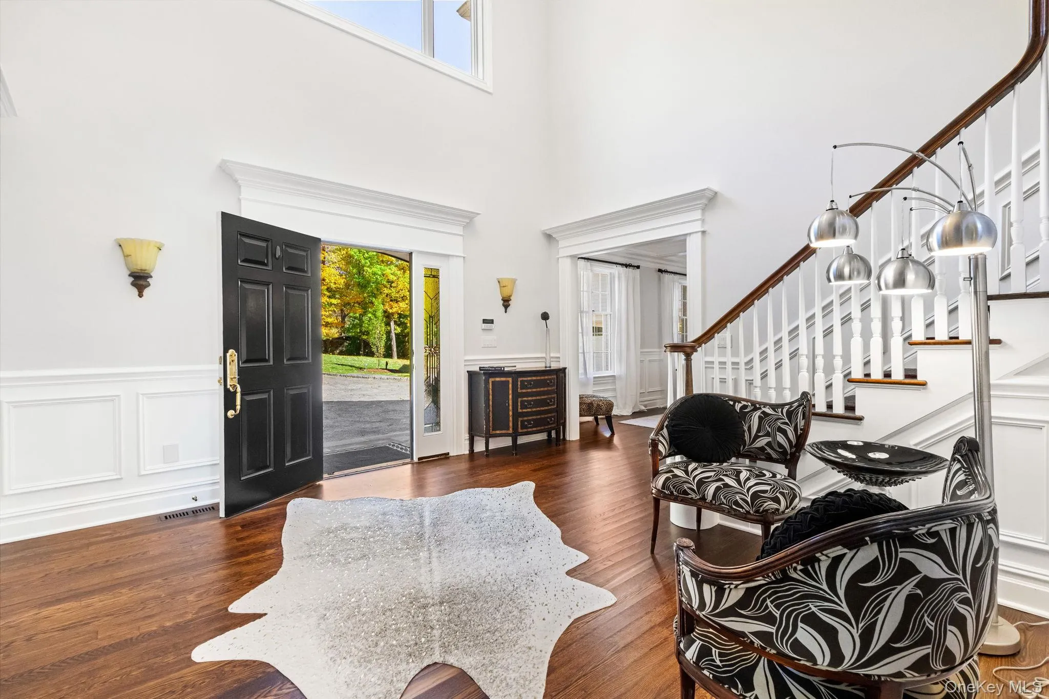 Foyer entrance with stairs, wood finished floors, a decorative wall, a towering ceiling, and a wainscoted wall Foyer entrance with stairs, wood finished floors, a decorative wall, a towering ceiling, and a wainscoted wall