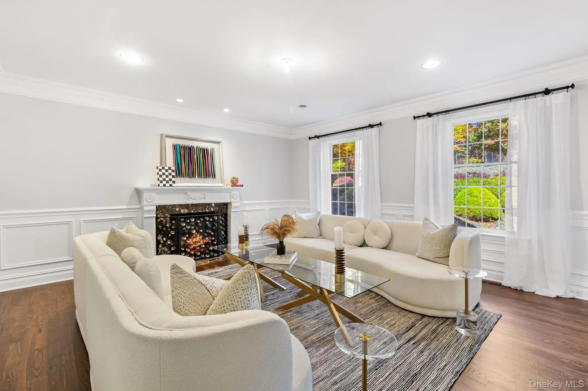 Living room featuring a high end fireplace, dark wood-style floors, ornamental molding, a decorative wall, and wainscoting Living room featuring a high end fireplace, dark wood-style floors, ornamental molding, a decorative wall, and wainscoting