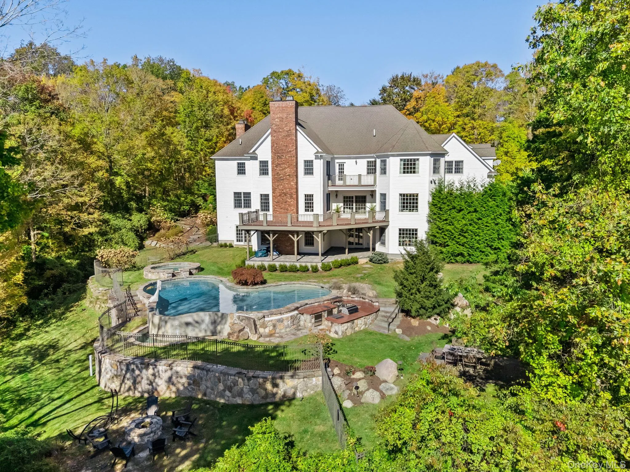 Back of house with a chimney, a lawn, a wooden deck, an outdoor fire pit, and a patio area Back of house with a chimney, a lawn, a wooden deck, an outdoor fire pit, and a patio area