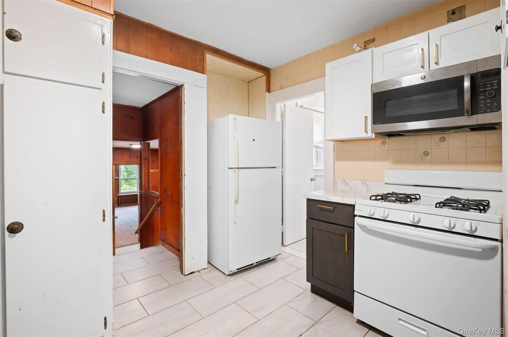 Kitchen with white appliances, light countertops, tasteful backsplash, light tile patterned floors, and white cabinets Kitchen with white appliances, light countertops, tasteful backsplash, light tile patterned floors, and white cabinets