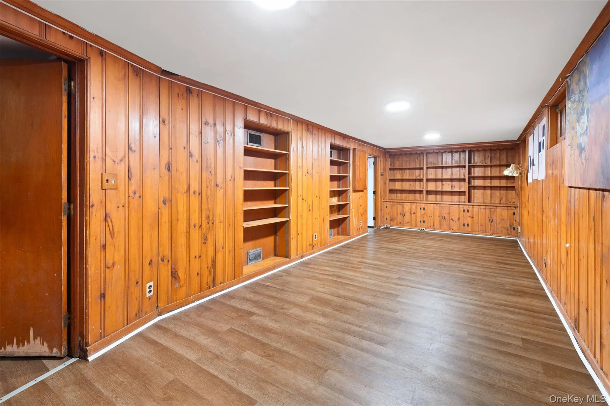 Empty room featuring wooden walls, wood finished floors, and built in shelves Empty room featuring wooden walls, wood finished floors, and built in shelves