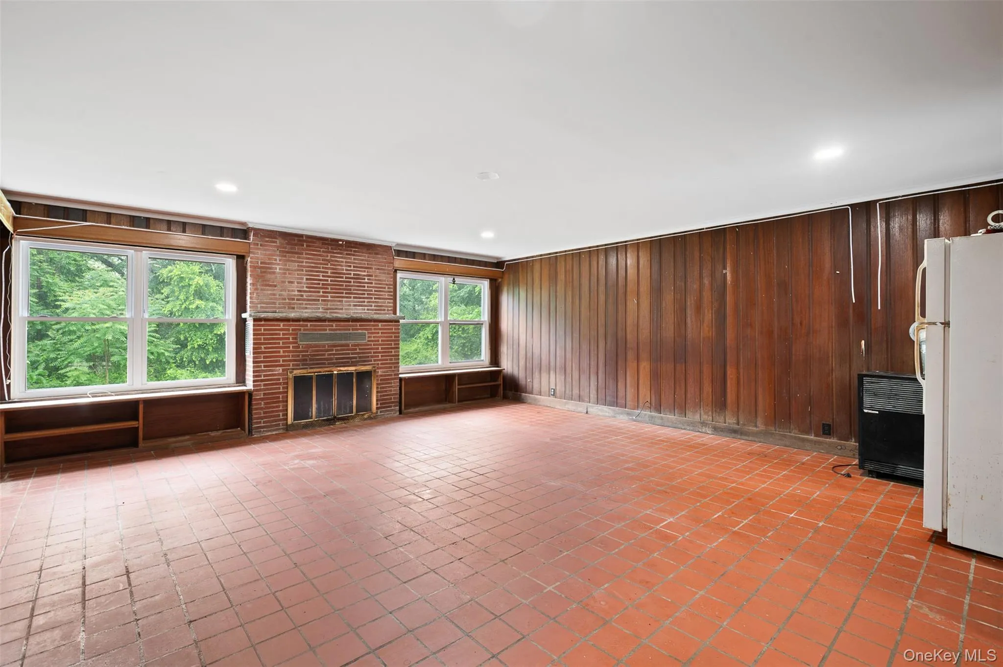 Unfurnished living room featuring wooden walls and a brick fireplace Unfurnished living room featuring wooden walls and a brick fireplace