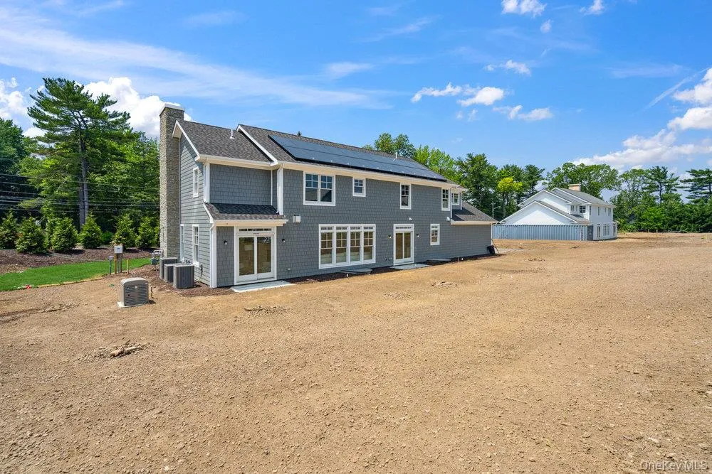 Back of house featuring solar panels, a chimney, and view of scattered trees Back of house featuring solar panels, a chimney, and view of scattered trees