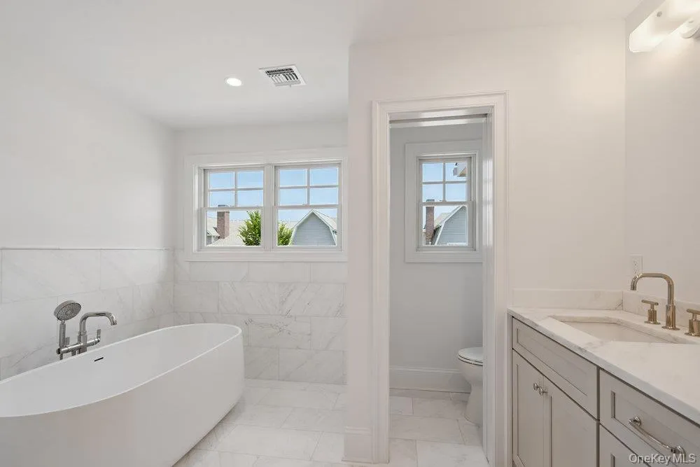 Bathroom featuring vanity, a freestanding bath, recessed lighting, light marble finish flooring, and tile walls Bathroom featuring vanity, a freestanding bath, recessed lighting, light marble finish flooring, and tile walls