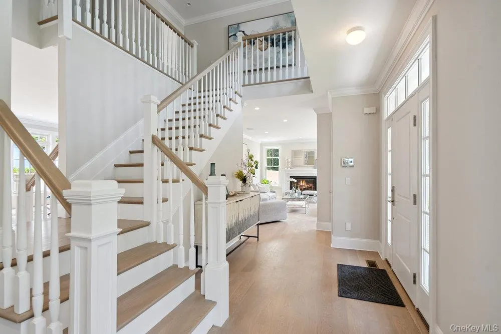 Entryway featuring ornamental molding, stairway, light wood-type flooring, a glass covered fireplace, and a towering ceiling Entryway featuring ornamental molding, stairway, light wood-type flooring, a glass covered fireplace, and a towering ceiling