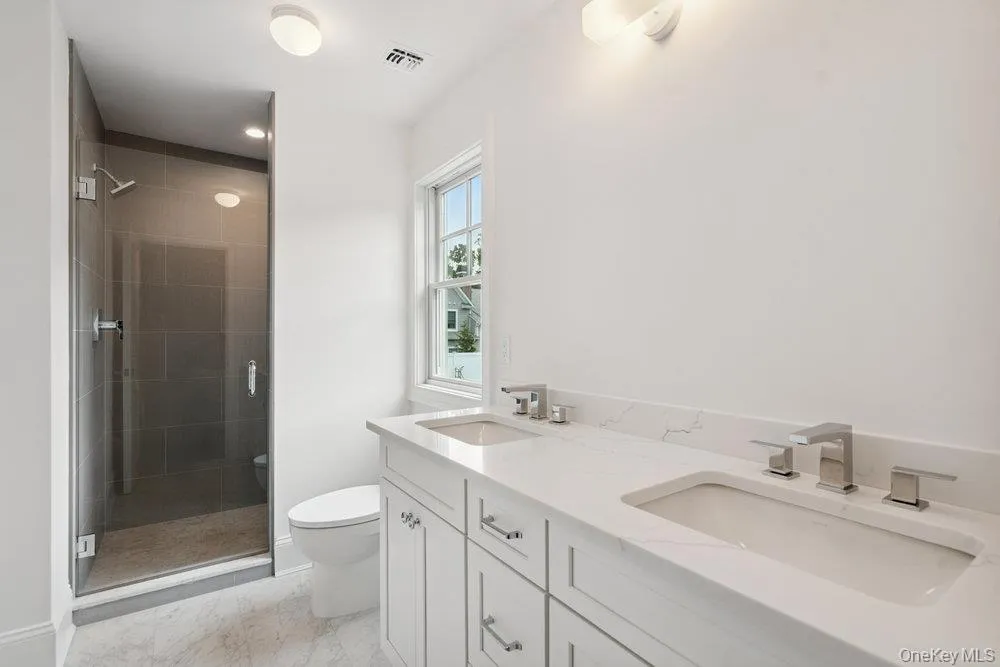 Full bathroom featuring double vanity, a stall shower, and light marble finish floors Full bathroom featuring double vanity, a stall shower, and light marble finish floors