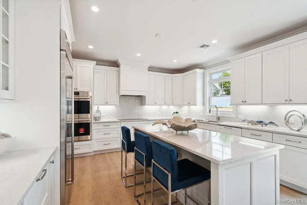 Kitchen with a breakfast bar, white cabinetry, light wood-style floors, light stone countertops, and recessed lighting Kitchen with a breakfast bar, white cabinetry, light wood-style floors, light stone countertops, and recessed lighting