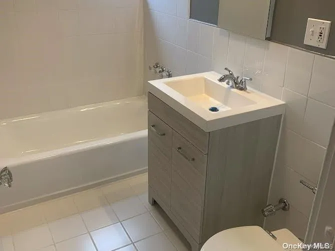 Bathroom featuring tile walls, vanity, light tile patterned floors, bathtub / shower combination, and tasteful backsplash Bathroom featuring tile walls, vanity, light tile patterned floors, bathtub / shower combination, and tasteful backsplash