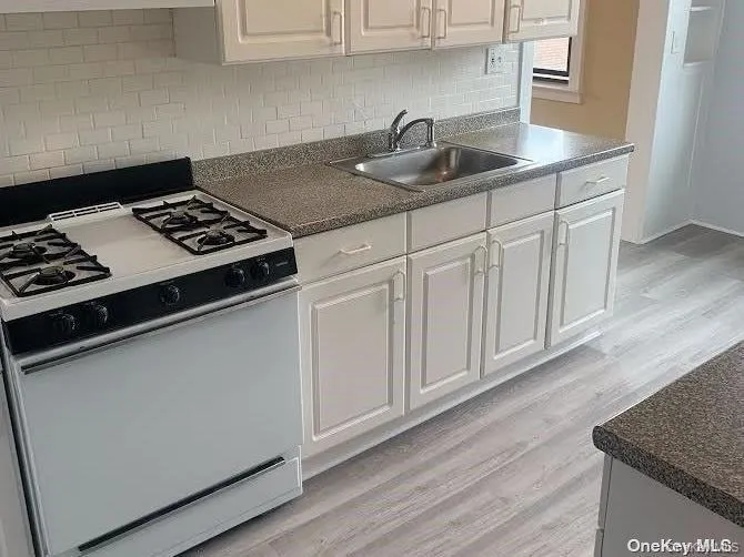 Kitchen featuring dark countertops, white range with gas cooktop, light wood-style flooring, decorative backsplash, and white cabinets Kitchen featuring dark countertops, white range with gas cooktop, light wood-style flooring, decorative backsplash, and white cabinets