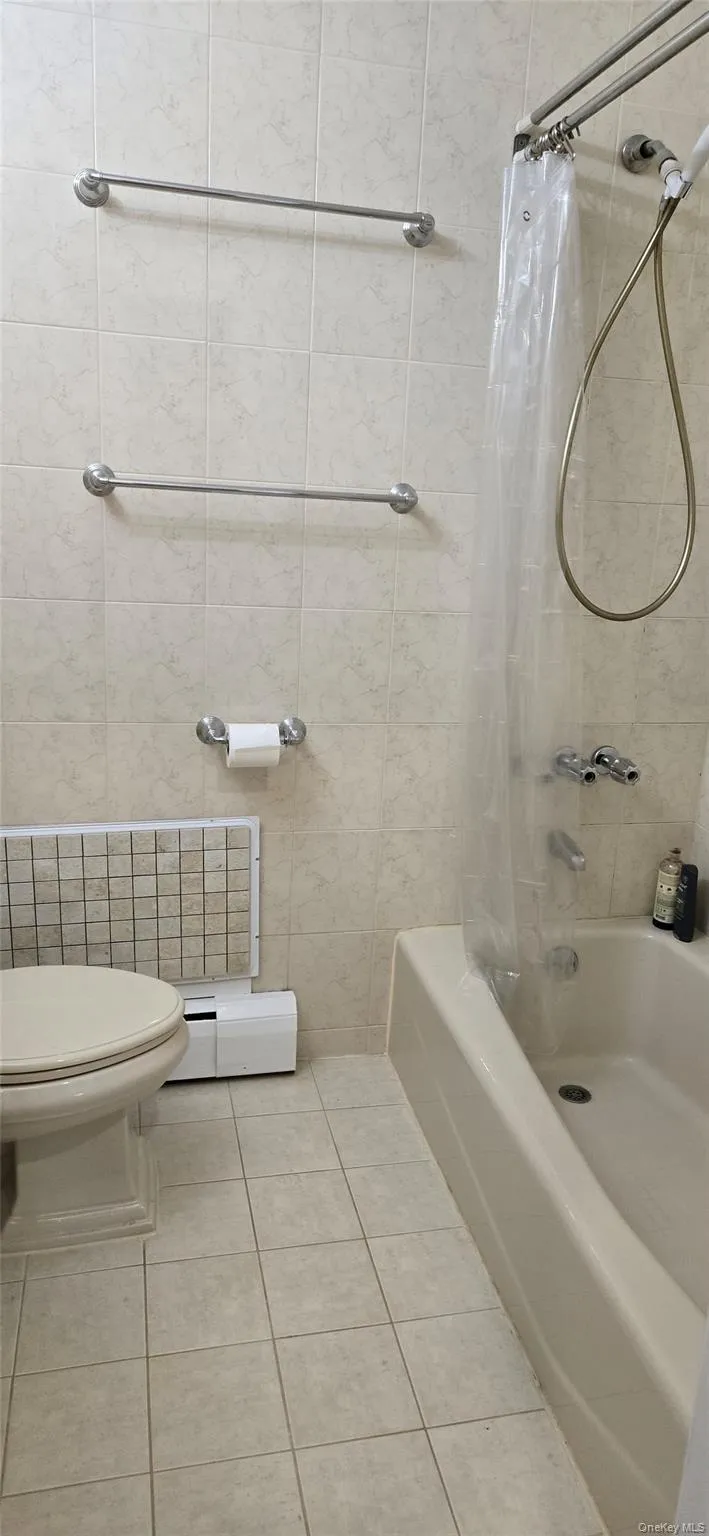 Full bathroom featuring shower / bath combination with curtain, baseboard heating, tile patterned flooring, and tile walls Full bathroom featuring shower / bath combination with curtain, baseboard heating, tile patterned flooring, and tile walls