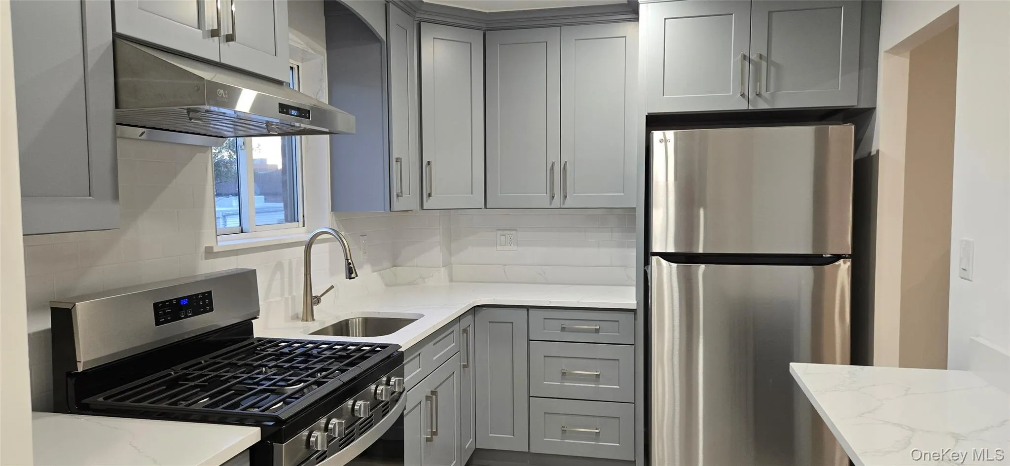 Kitchen with stainless steel appliances, gray cabinets, light stone counters, and tasteful backsplash Kitchen with stainless steel appliances, gray cabinets, light stone counters, and tasteful backsplash