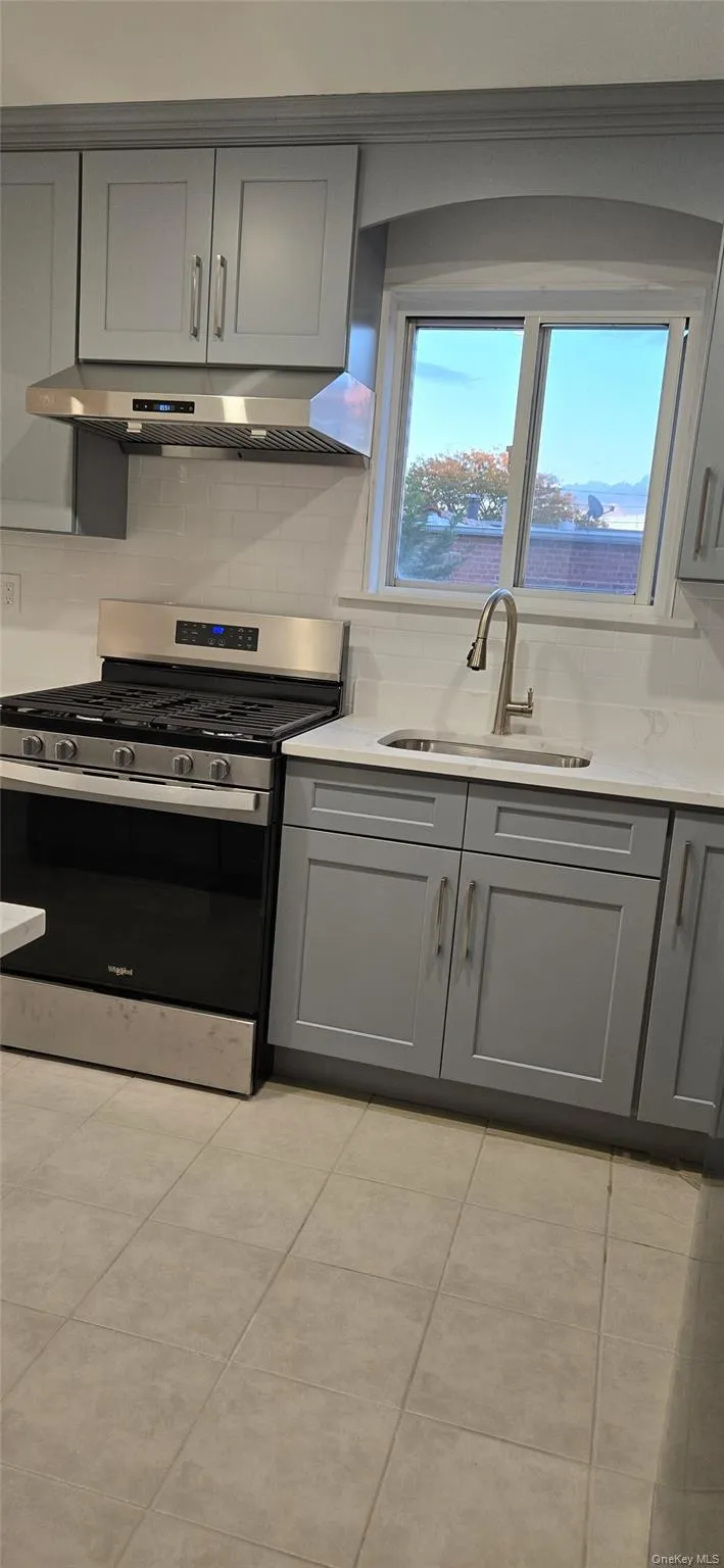 Kitchen featuring gray cabinets, stainless steel range with gas cooktop, backsplash, and under cabinet range hood Kitchen featuring gray cabinets, stainless steel range with gas cooktop, backsplash, and under cabinet range hood