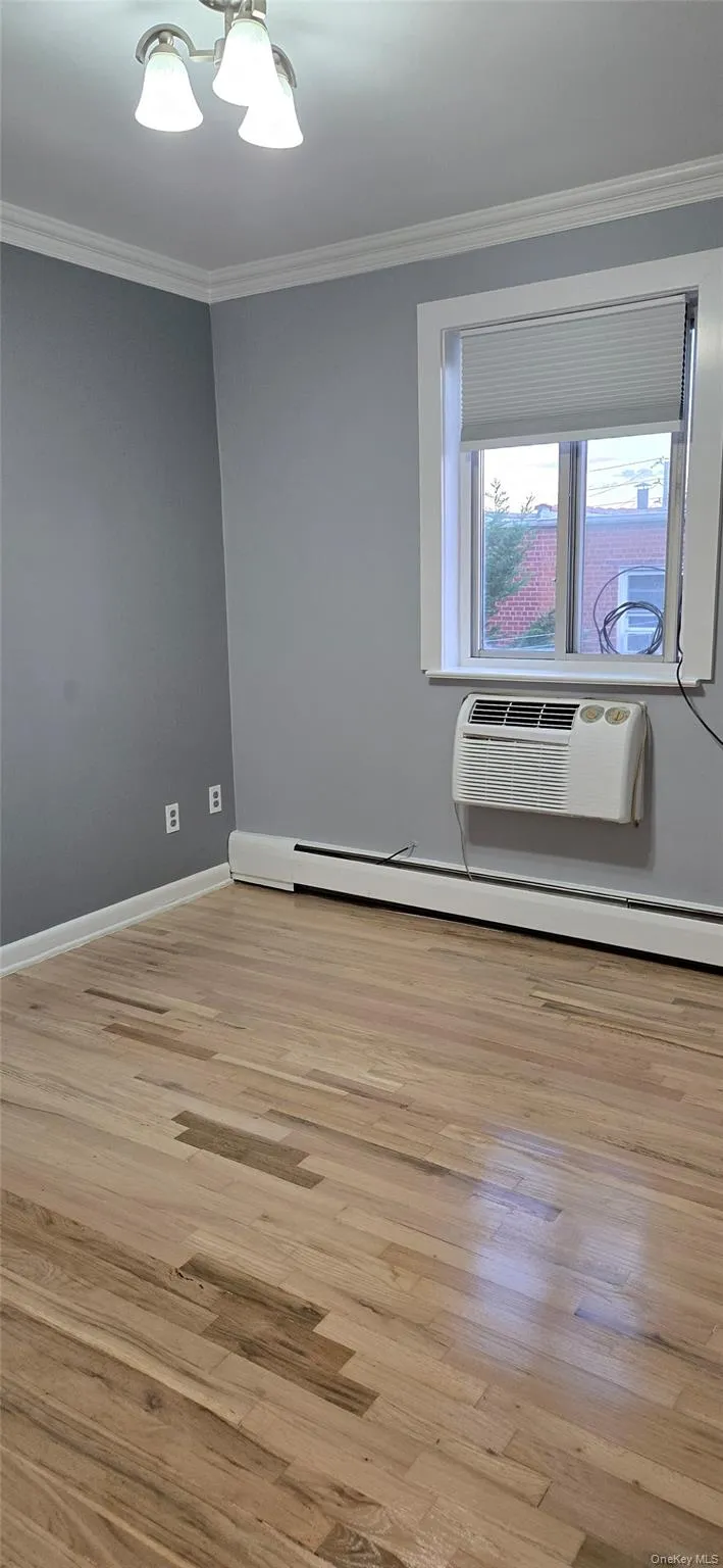Unfurnished room with ornamental molding, light wood finished floors, a baseboard heating unit, and a wall mounted AC Unfurnished room with ornamental molding, light wood finished floors, a baseboard heating unit, and a wall mounted AC