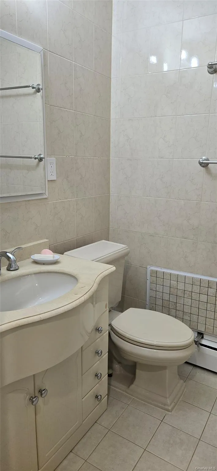 Bathroom featuring tile walls, vanity, light tile patterned floors, and a baseboard radiator Bathroom featuring tile walls, vanity, light tile patterned floors, and a baseboard radiator
