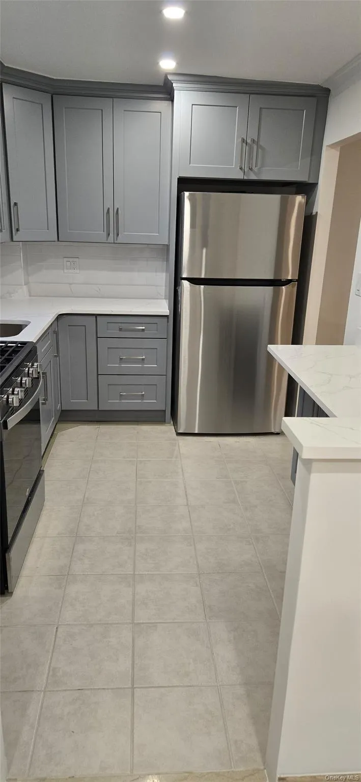 Kitchen featuring gray cabinets, light stone counters, freestanding refrigerator, black gas stove, and light tile patterned flooring Kitchen featuring gray cabinets, light stone counters, freestanding refrigerator, black gas stove, and light tile patterned flooring