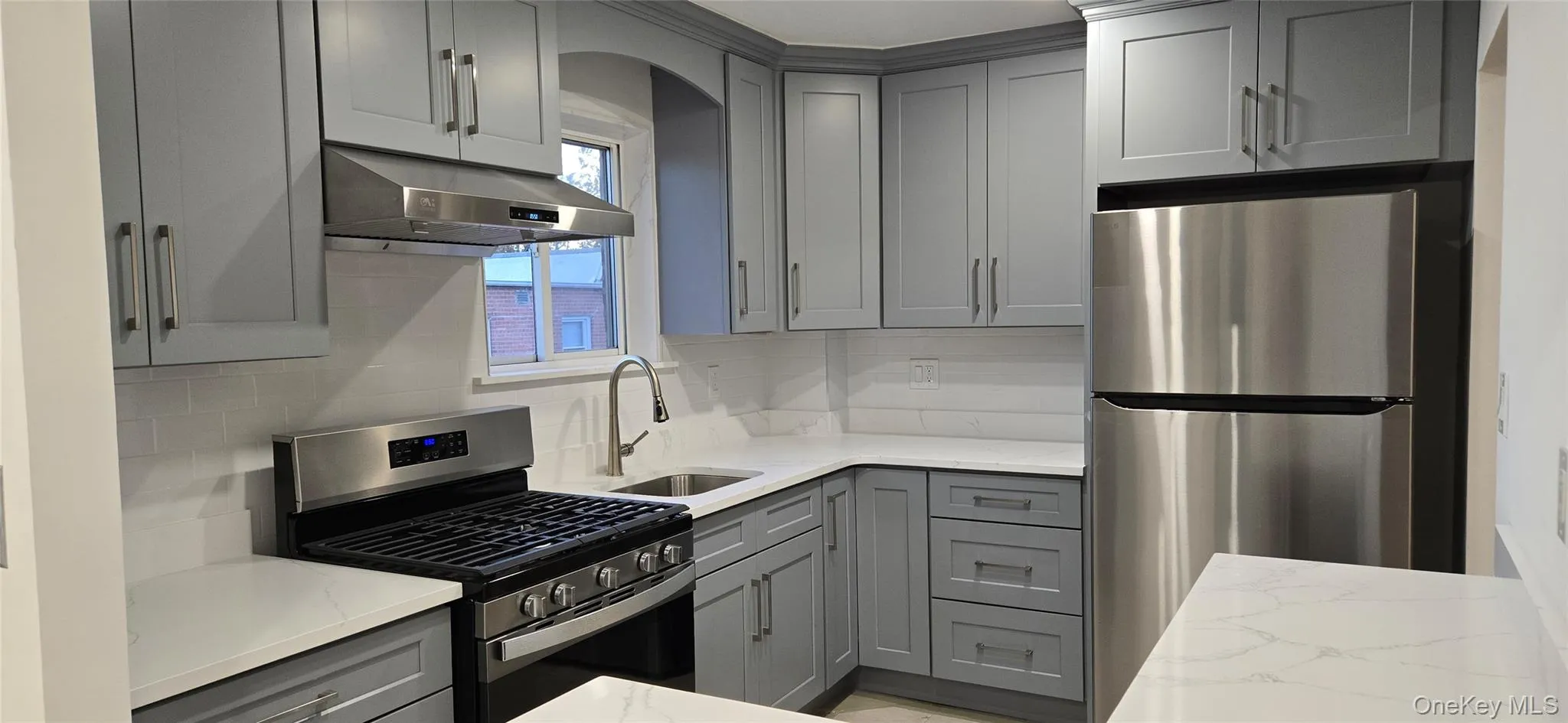 Kitchen with gray cabinets, stainless steel appliances, light stone countertops, tasteful backsplash, and under cabinet range hood Kitchen with gray cabinets, stainless steel appliances, light stone countertops, tasteful backsplash, and under cabinet range hood