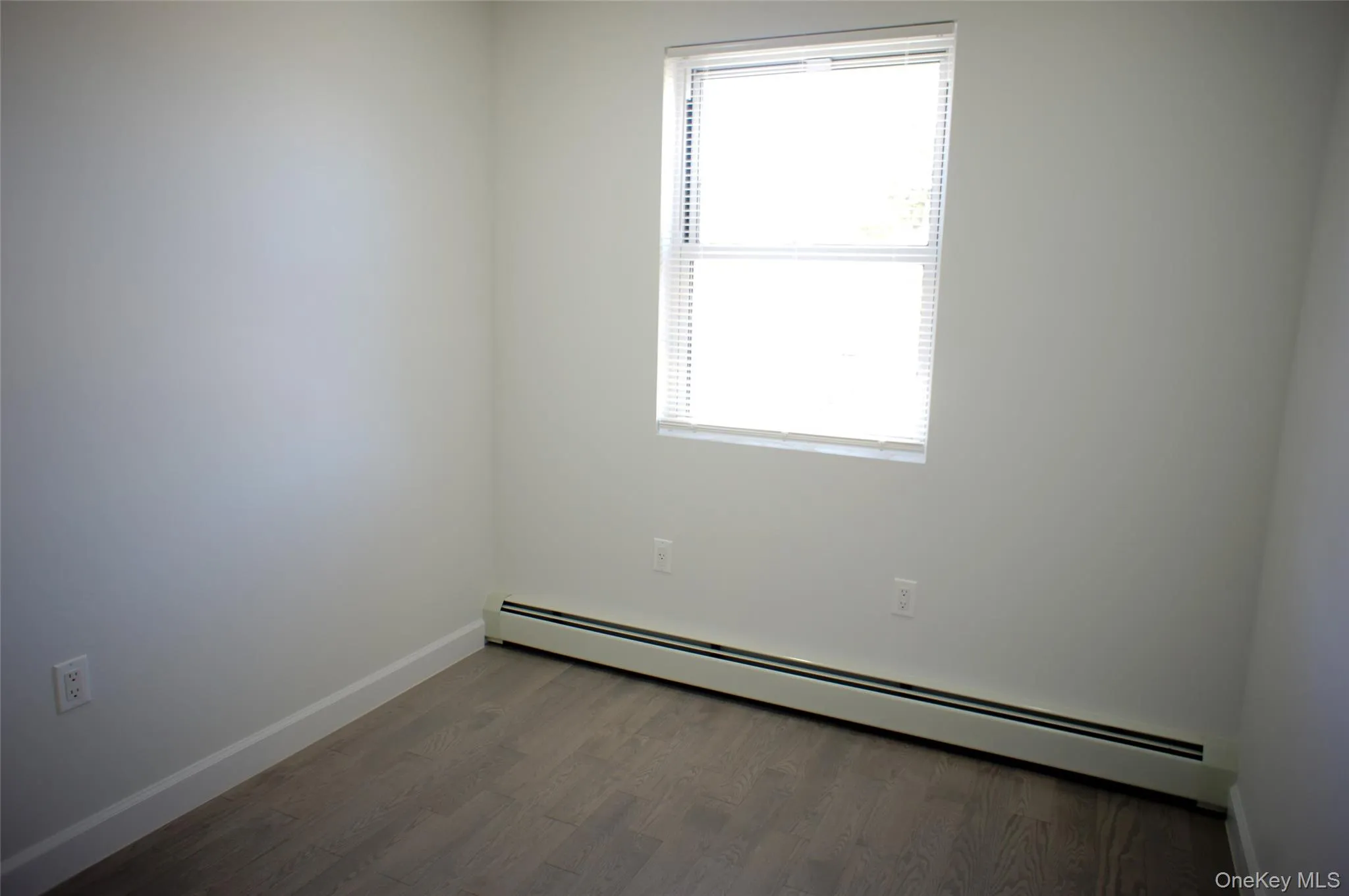 Unfurnished room with a baseboard radiator and wood finished floors Unfurnished room with a baseboard radiator and wood finished floors