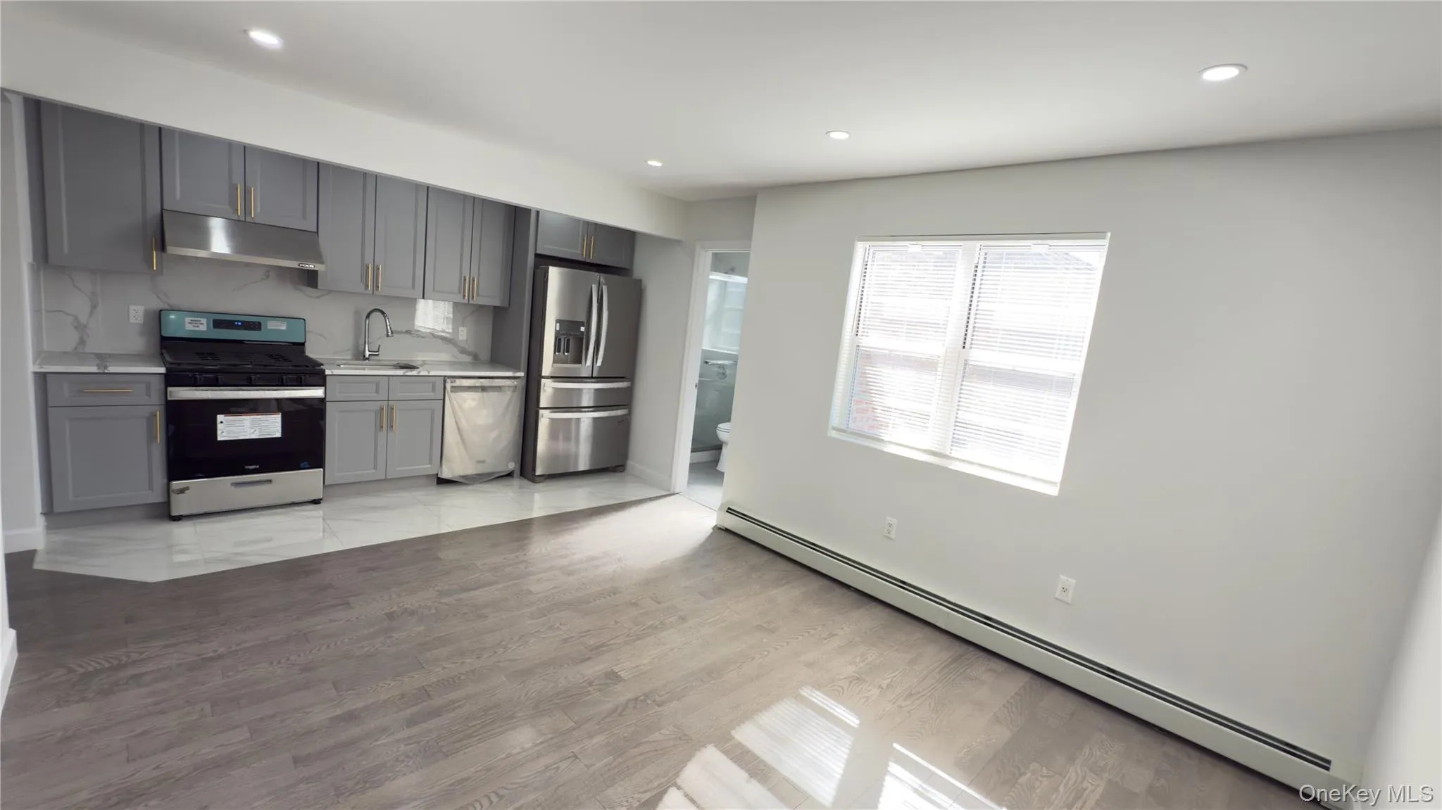 Kitchen with a baseboard radiator, gray cabinets, stainless steel appliances, recessed lighting, and under cabinet range hood Kitchen with a baseboard radiator, gray cabinets, stainless steel appliances, recessed lighting, and under cabinet range hood