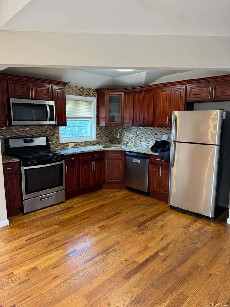 Kitchen with appliances with stainless steel finishes, backsplash, dark wood-style floors, glass insert cabinets, and light stone countertops Kitchen with appliances with stainless steel finishes, backsplash, dark wood-style floors, glass insert cabinets, and light stone countertops