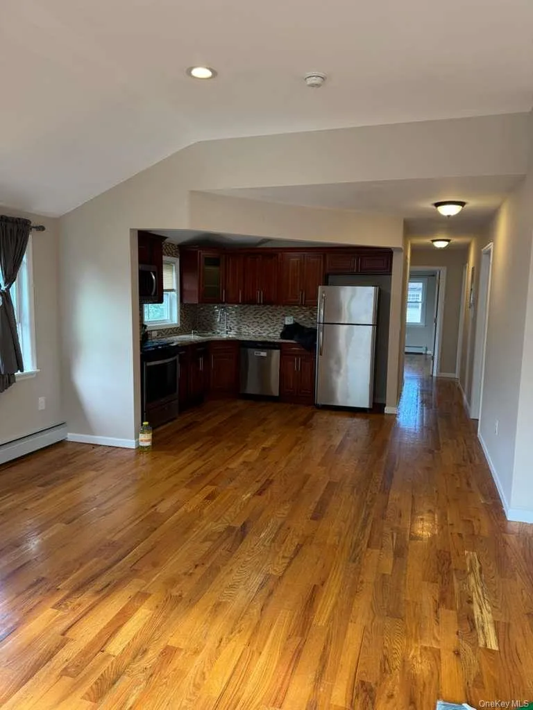 Kitchen with appliances with stainless steel finishes, tasteful backsplash, dark wood-style flooring, a baseboard radiator, and lofted ceiling Kitchen with appliances with stainless steel finishes, tasteful backsplash, dark wood-style flooring, a baseboard radiator, and lofted ceiling