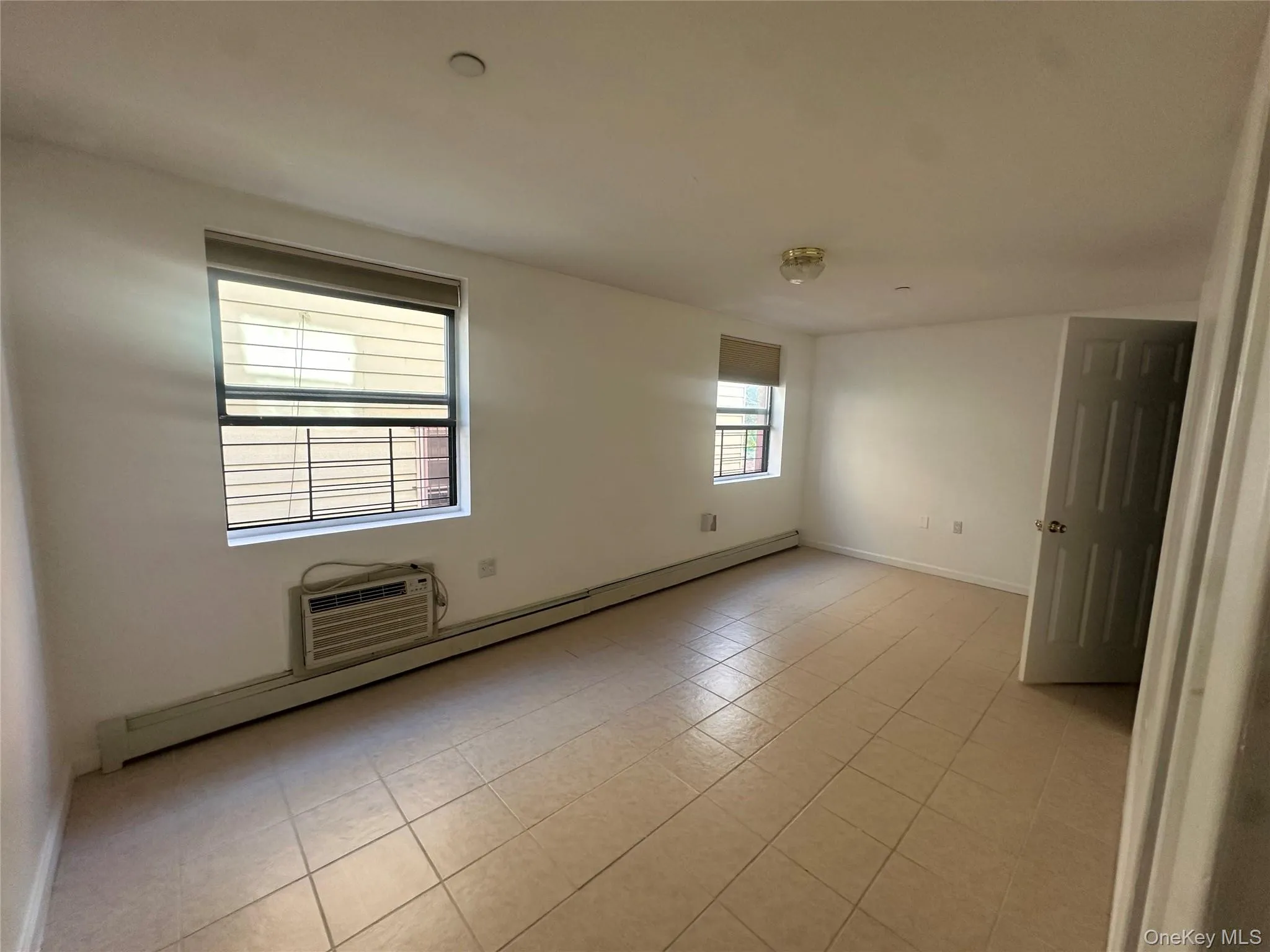 Empty room featuring a baseboard radiator, light tile patterned floors, and a wall mounted air conditioner Empty room featuring a baseboard radiator, light tile patterned floors, and a wall mounted air conditioner