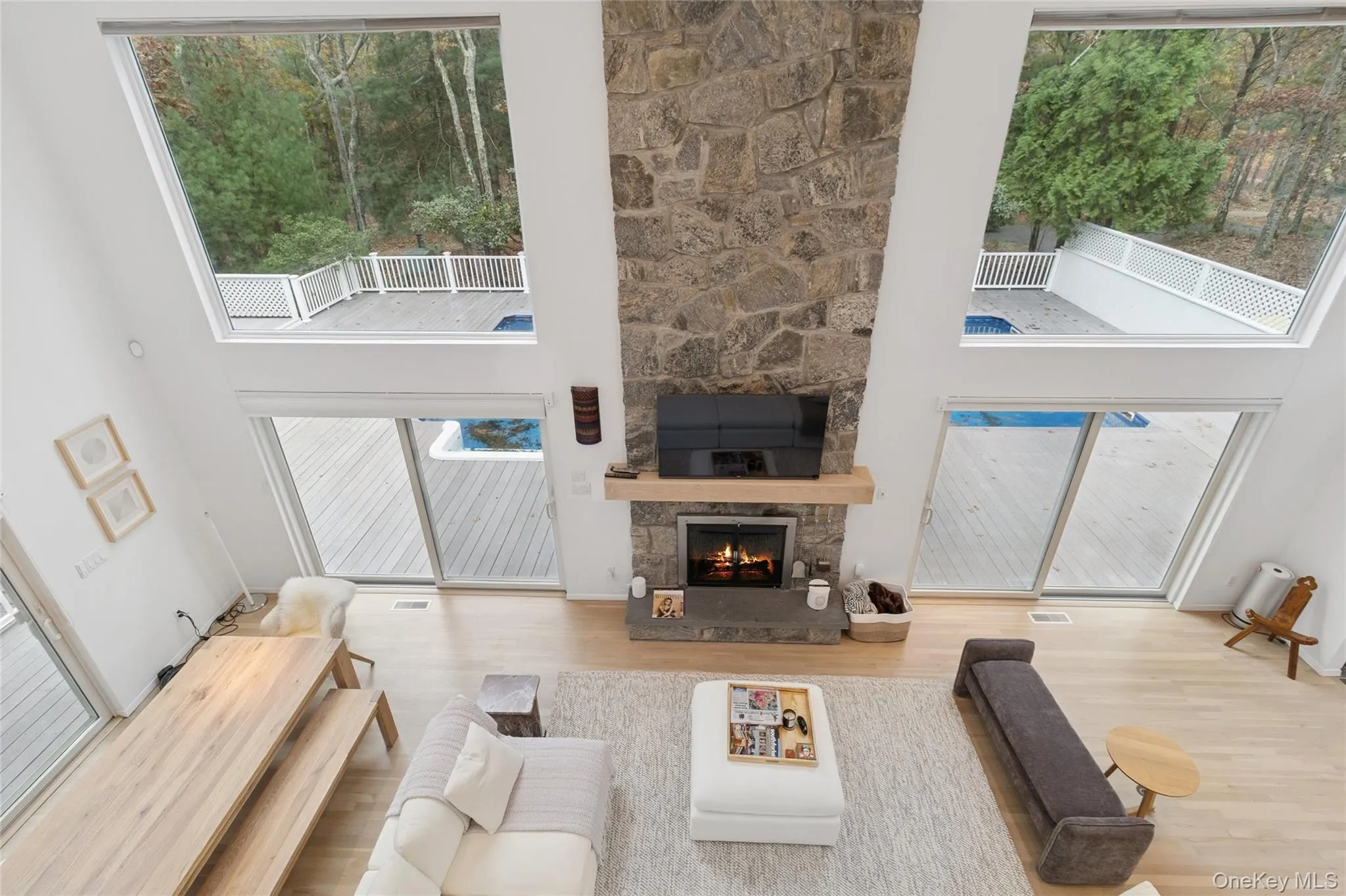 Living room featuring a high ceiling, healthy amount of natural light, a stone fireplace, and wood finished floors Living room featuring a high ceiling, healthy amount of natural light, a stone fireplace, and wood finished floors