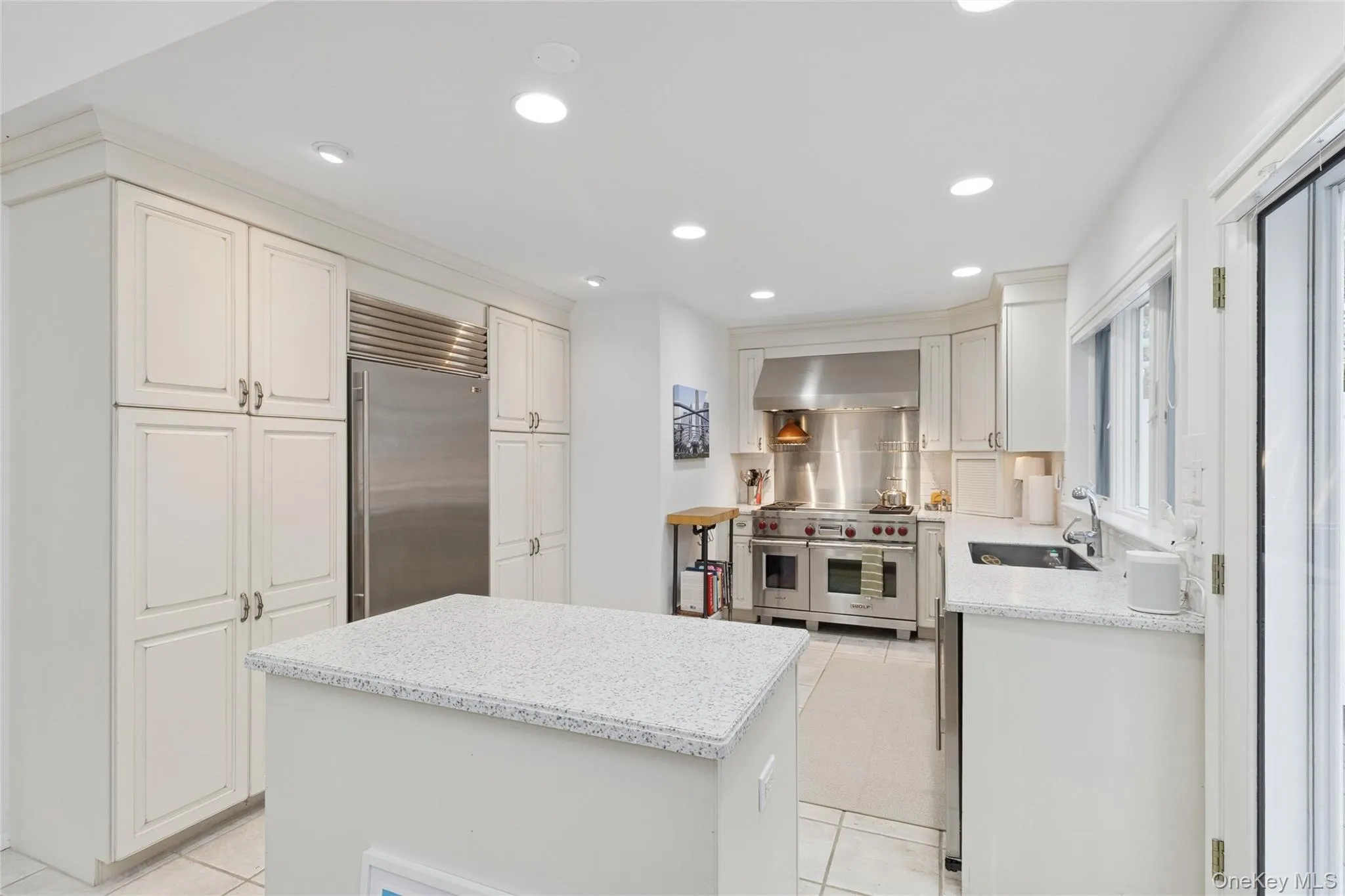 Kitchen with white cabinetry, premium appliances, recessed lighting, wall chimney exhaust hood, and a kitchen island Kitchen with white cabinetry, premium appliances, recessed lighting, wall chimney exhaust hood, and a kitchen island