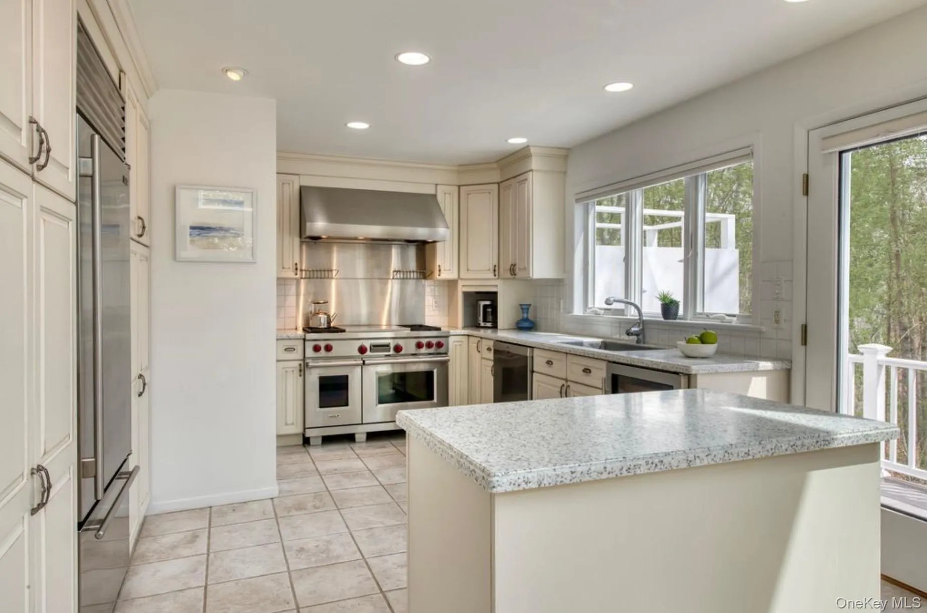 Kitchen with cream cabinetry, high quality appliances, tasteful backsplash, wall chimney range hood, and recessed lighting Kitchen with cream cabinetry, high quality appliances, tasteful backsplash, wall chimney range hood, and recessed lighting