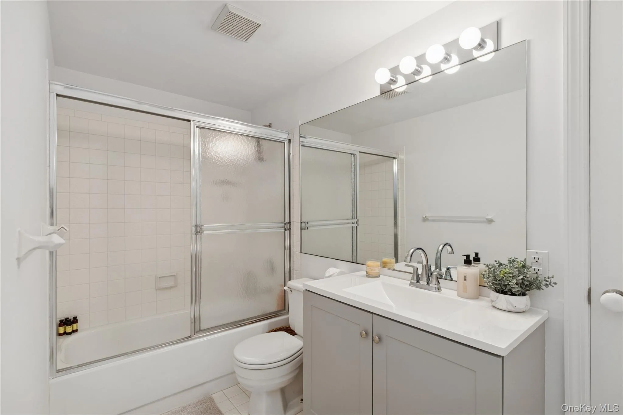 Full bathroom with enclosed tub / shower combo, vanity, and light tile patterned floors Full bathroom with enclosed tub / shower combo, vanity, and light tile patterned floors