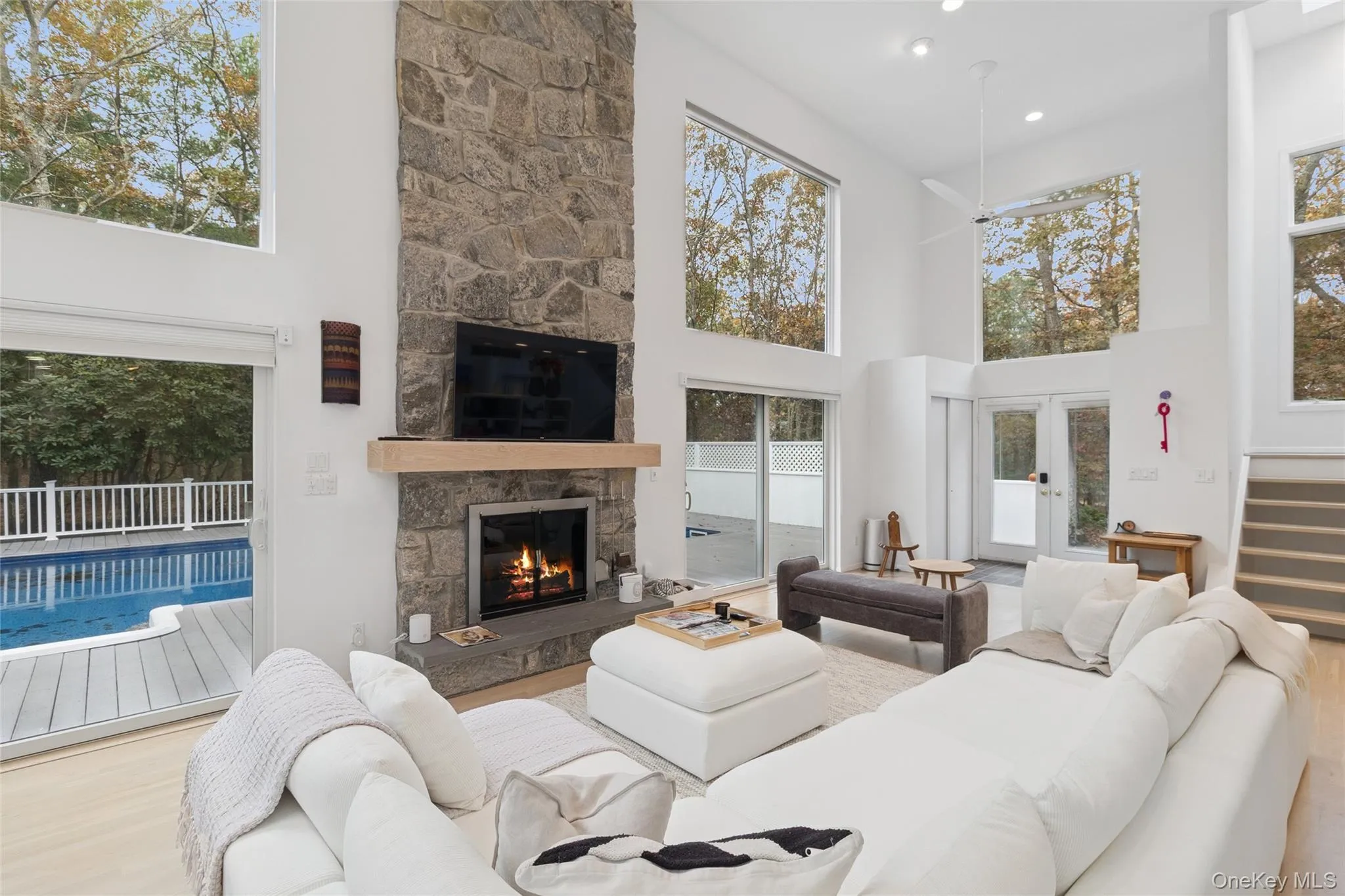 Living room featuring a high ceiling, wood finished floors, a stone fireplace, and ceiling fan Living room featuring a high ceiling, wood finished floors, a stone fireplace, and ceiling fan