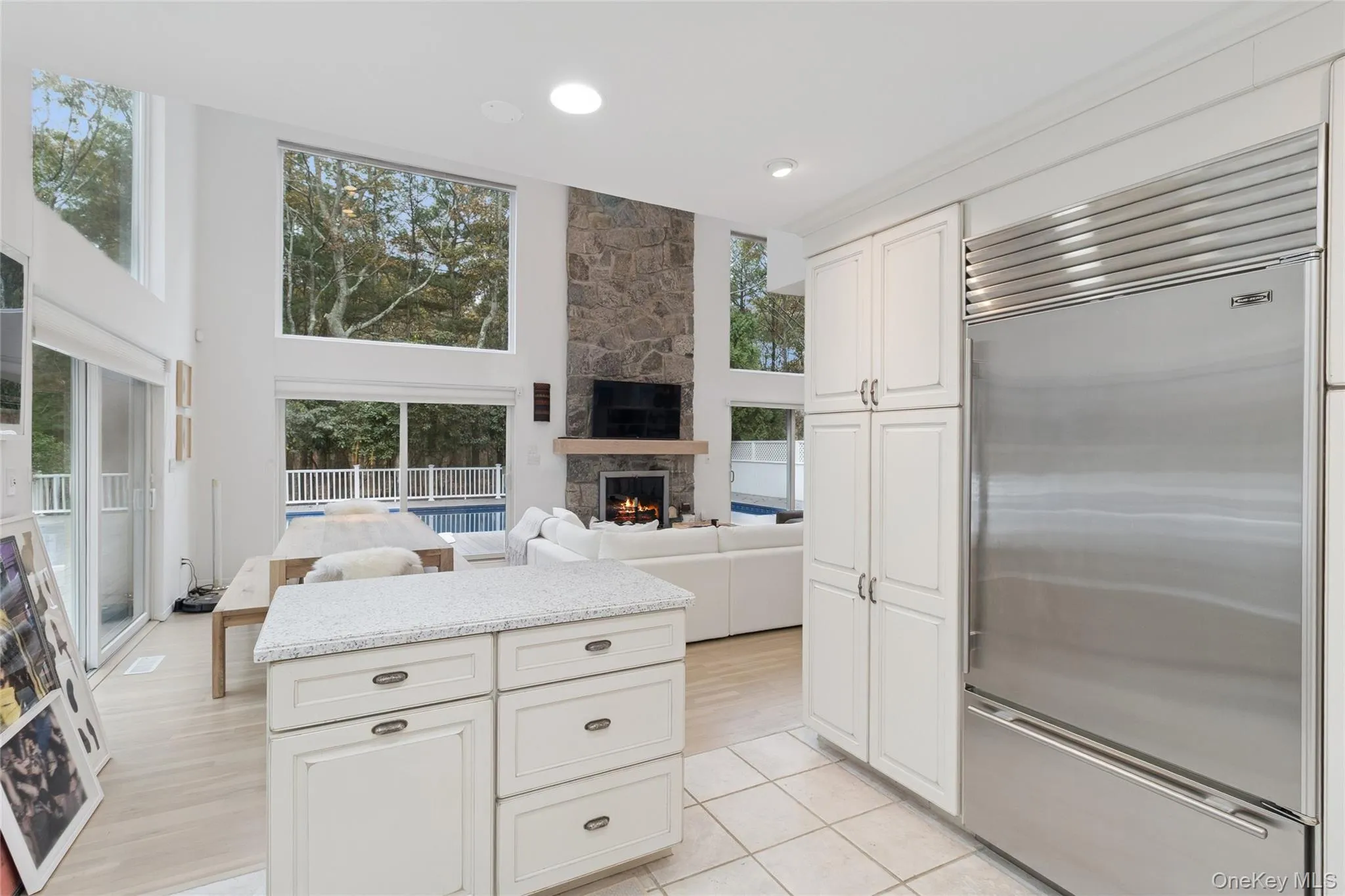 Kitchen with built in refrigerator, white cabinets, open floor plan, light stone counters, and a stone fireplace Kitchen with built in refrigerator, white cabinets, open floor plan, light stone counters, and a stone fireplace