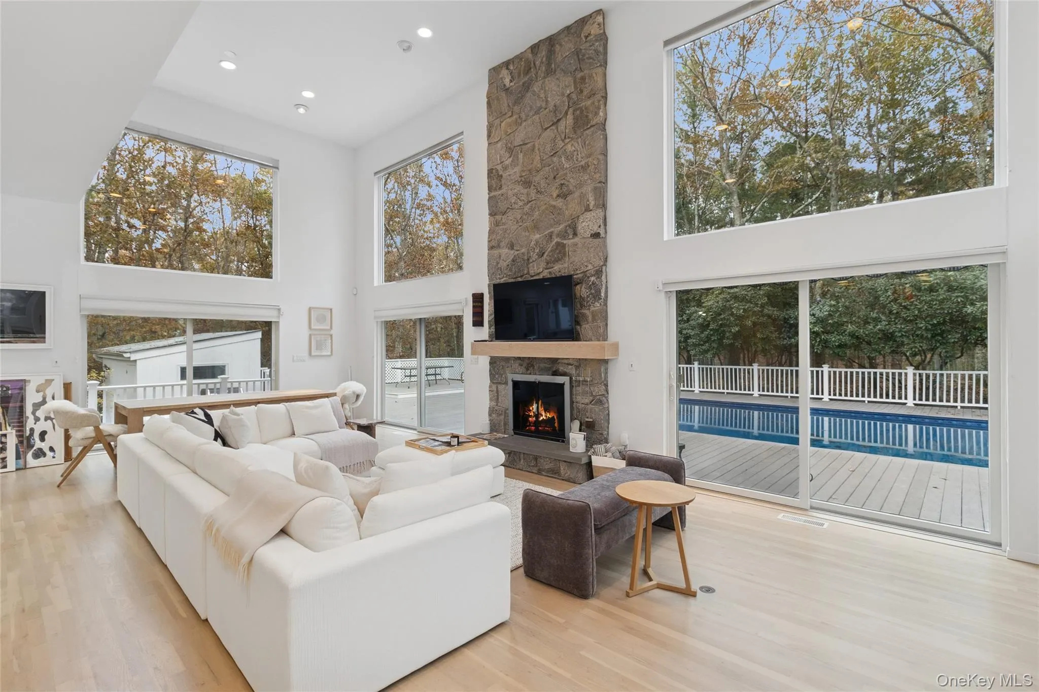 Living room with a high ceiling, light wood-style flooring, a fireplace, and recessed lighting Living room with a high ceiling, light wood-style flooring, a fireplace, and recessed lighting
