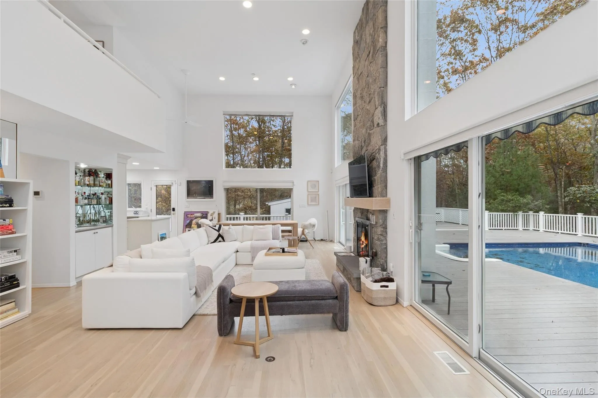 Living area featuring recessed lighting, a high ceiling, a stone fireplace, and light wood finished floors Living area featuring recessed lighting, a high ceiling, a stone fireplace, and light wood finished floors