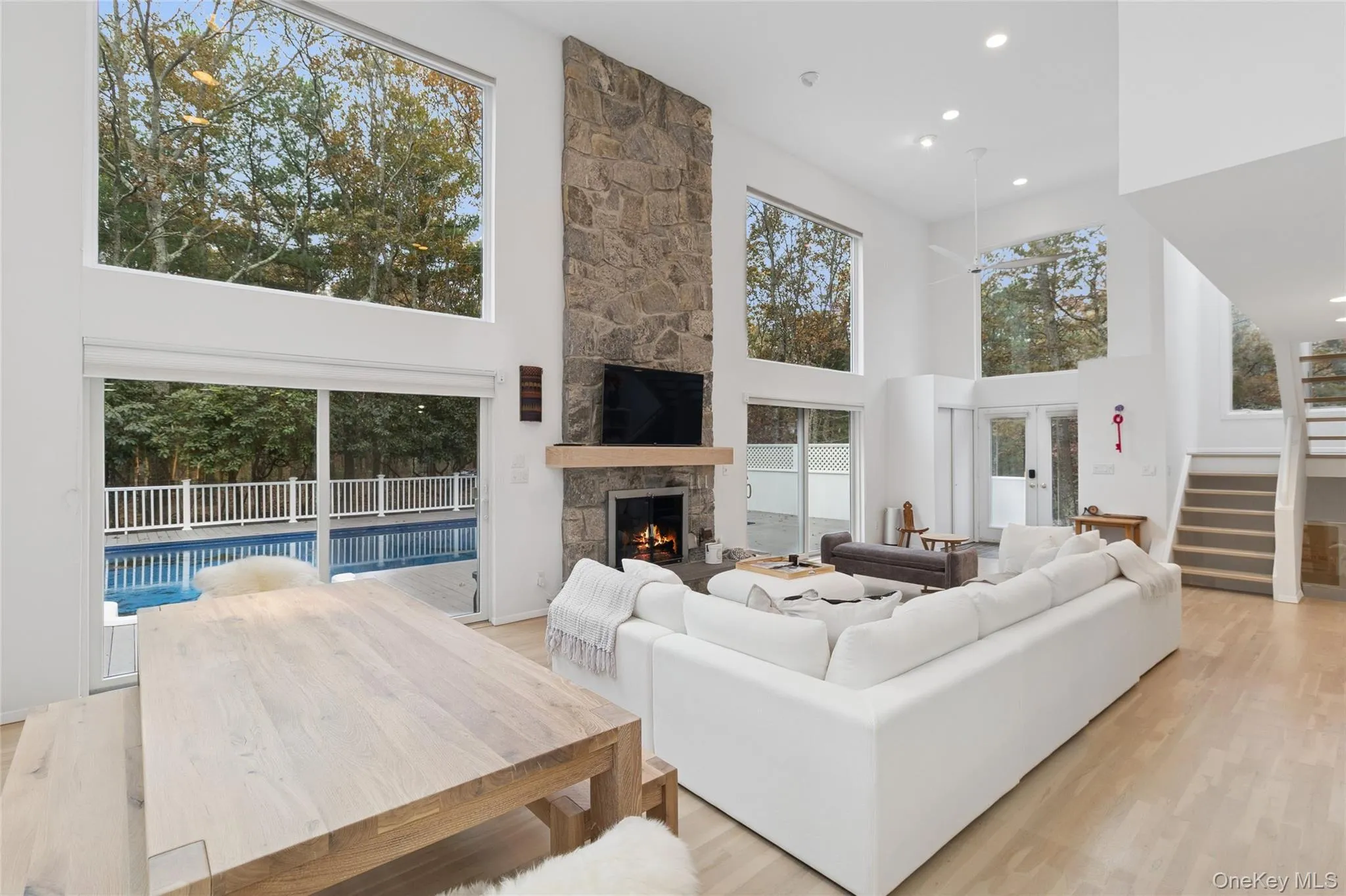 Living area featuring a towering ceiling, light wood-style flooring, a fireplace, recessed lighting, and stairs Living area featuring a towering ceiling, light wood-style flooring, a fireplace, recessed lighting, and stairs