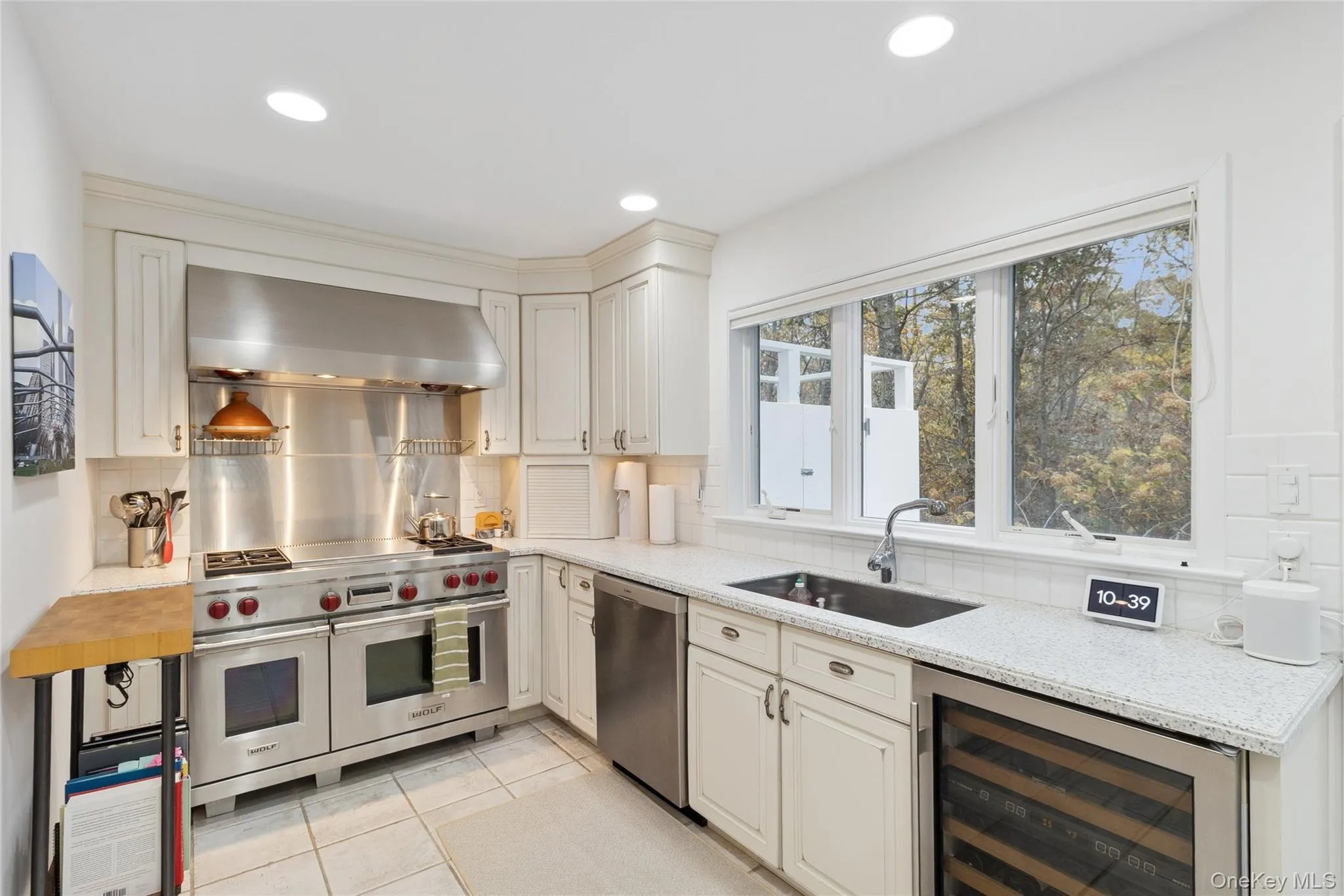 Kitchen featuring appliances with stainless steel finishes, range hood, beverage cooler, light stone counters, and light tile patterned floors Kitchen featuring appliances with stainless steel finishes, range hood, beverage cooler, light stone counters, and light tile patterned floors
