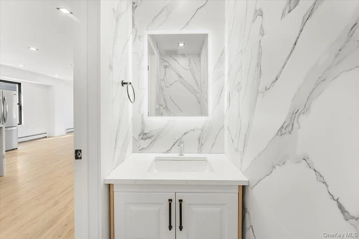 Half bathroom featuring vanity, baseboard heating, recessed lighting, and wood finished floors Half bathroom featuring vanity, baseboard heating, recessed lighting, and wood finished floors