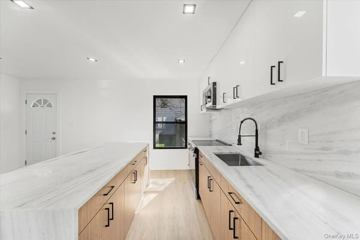 Kitchen featuring modern cabinets, light stone countertops, light wood-style flooring, stainless steel appliances, and white cabinets Kitchen featuring modern cabinets, light stone countertops, light wood-style flooring, stainless steel appliances, and white cabinets