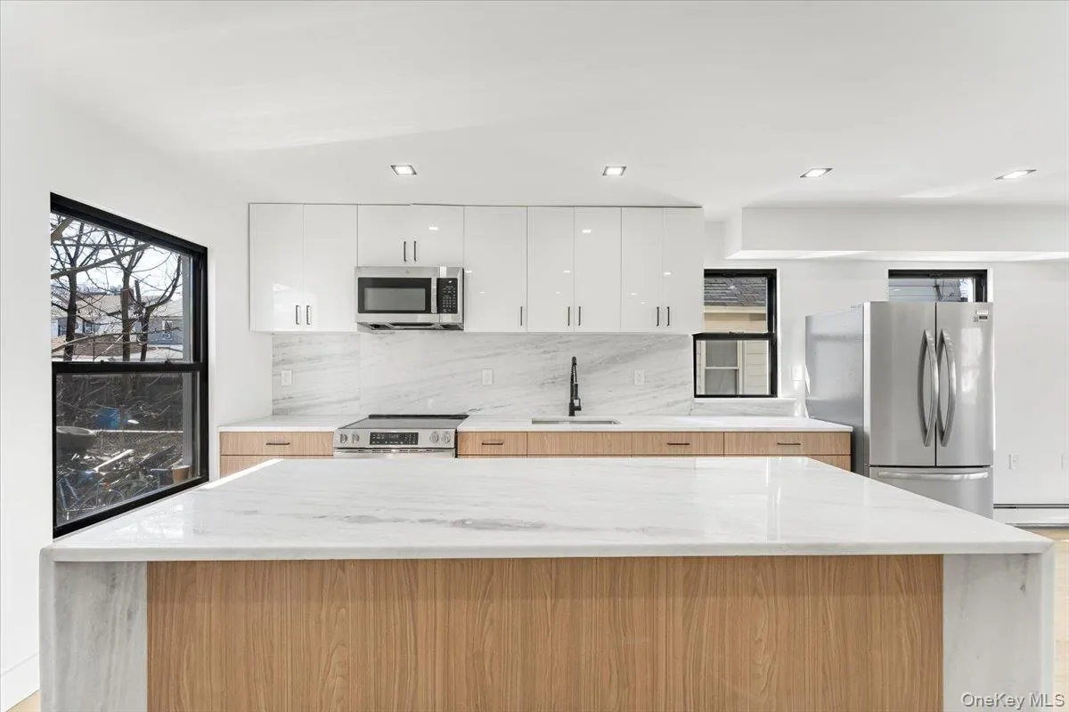 Kitchen with light stone countertops, white cabinets, appliances with stainless steel finishes, modern cabinets, and backsplash Kitchen with light stone countertops, white cabinets, appliances with stainless steel finishes, modern cabinets, and backsplash