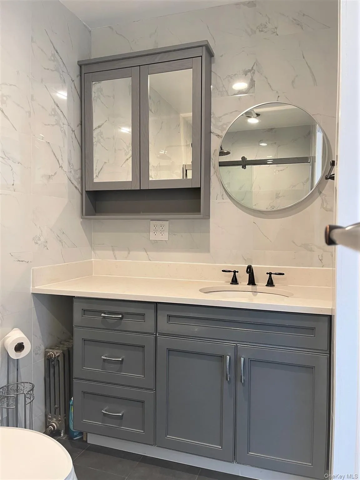 Bathroom featuring vanity, a marble finish shower, dark tile patterned flooring, radiator heating unit, and tile walls Bathroom featuring vanity, a marble finish shower, dark tile patterned flooring, radiator heating unit, and tile walls