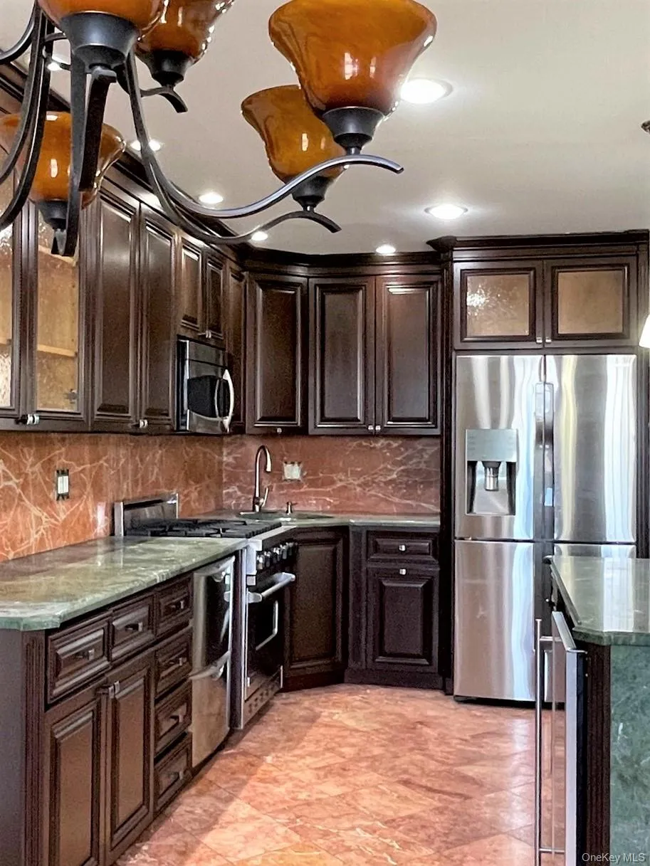Kitchen with glass insert cabinets, dark brown cabinets, appliances with stainless steel finishes, tasteful backsplash, and recessed lighting Kitchen with glass insert cabinets, dark brown cabinets, appliances with stainless steel finishes, tasteful backsplash, and recessed lighting